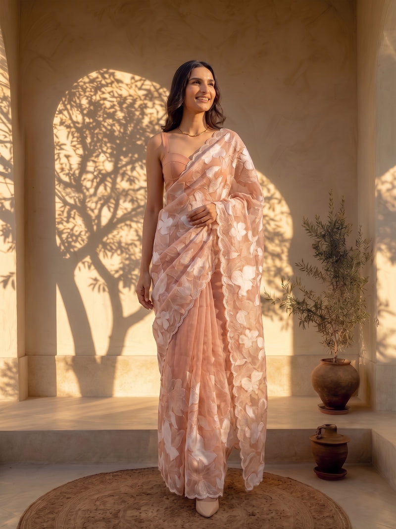 Woman in a floral saree standing in a sunlit room with shadows on the wall.