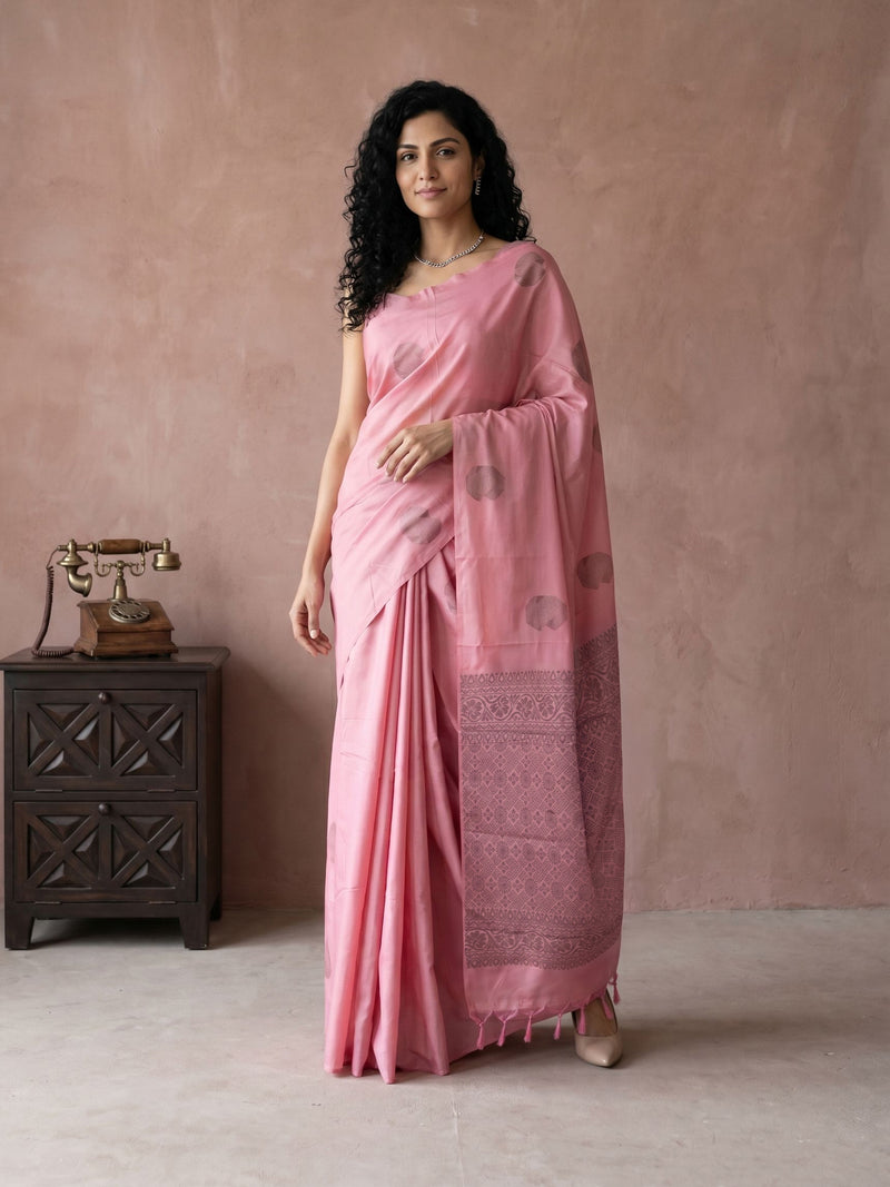 Woman in a pink saree standing against a beige wall with a wooden side table and vintage phone.