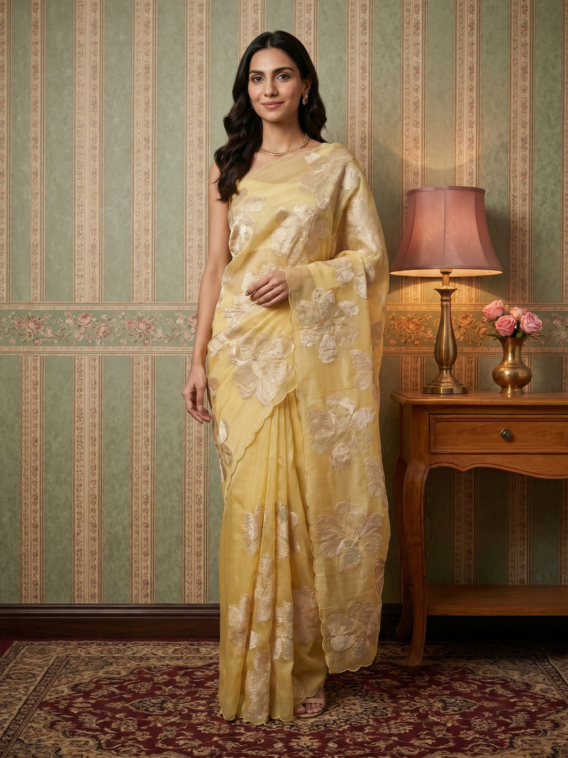 Woman in a yellow saree standing in a room with a lamp and vase on a table.