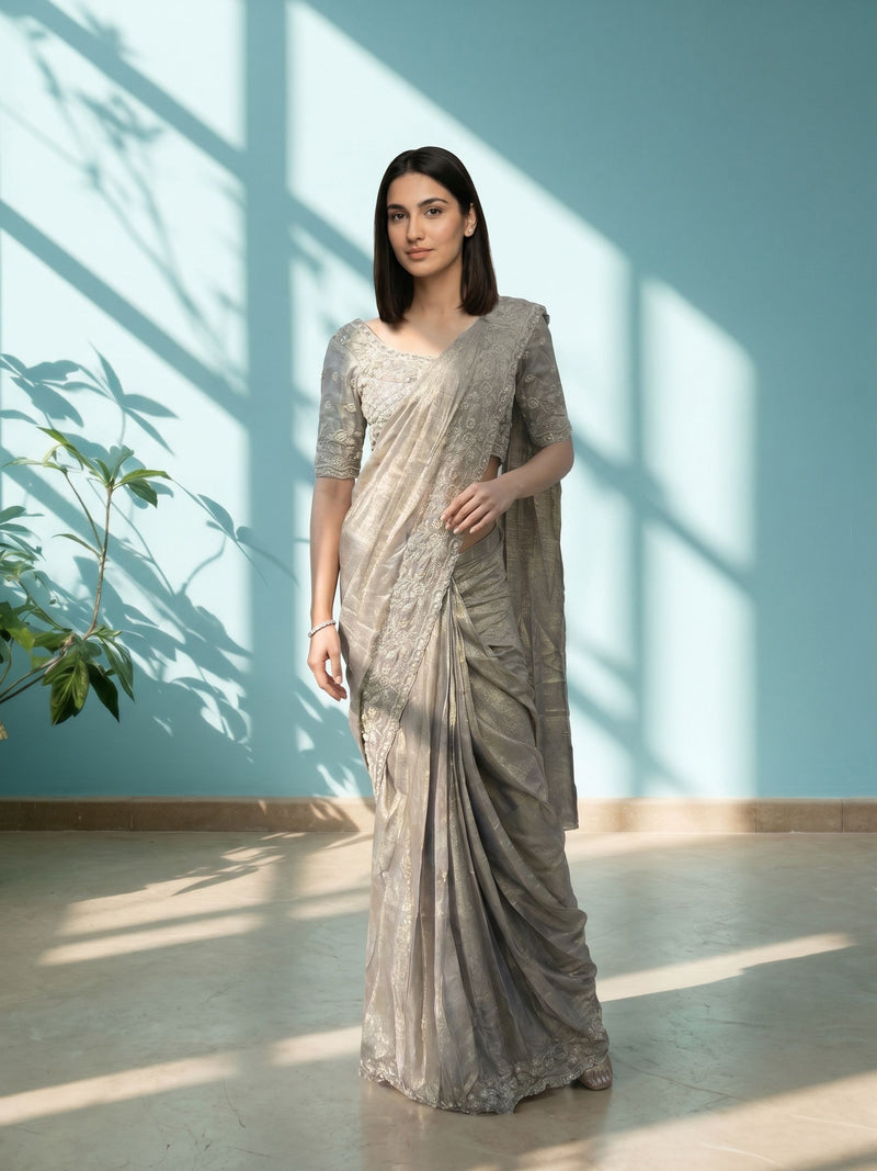 Woman in a silver saree standing in a room with a blue wall and plant.