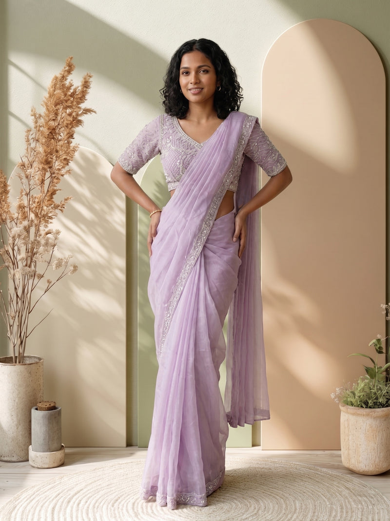 Woman in a lavender saree standing indoors with decorative plants.