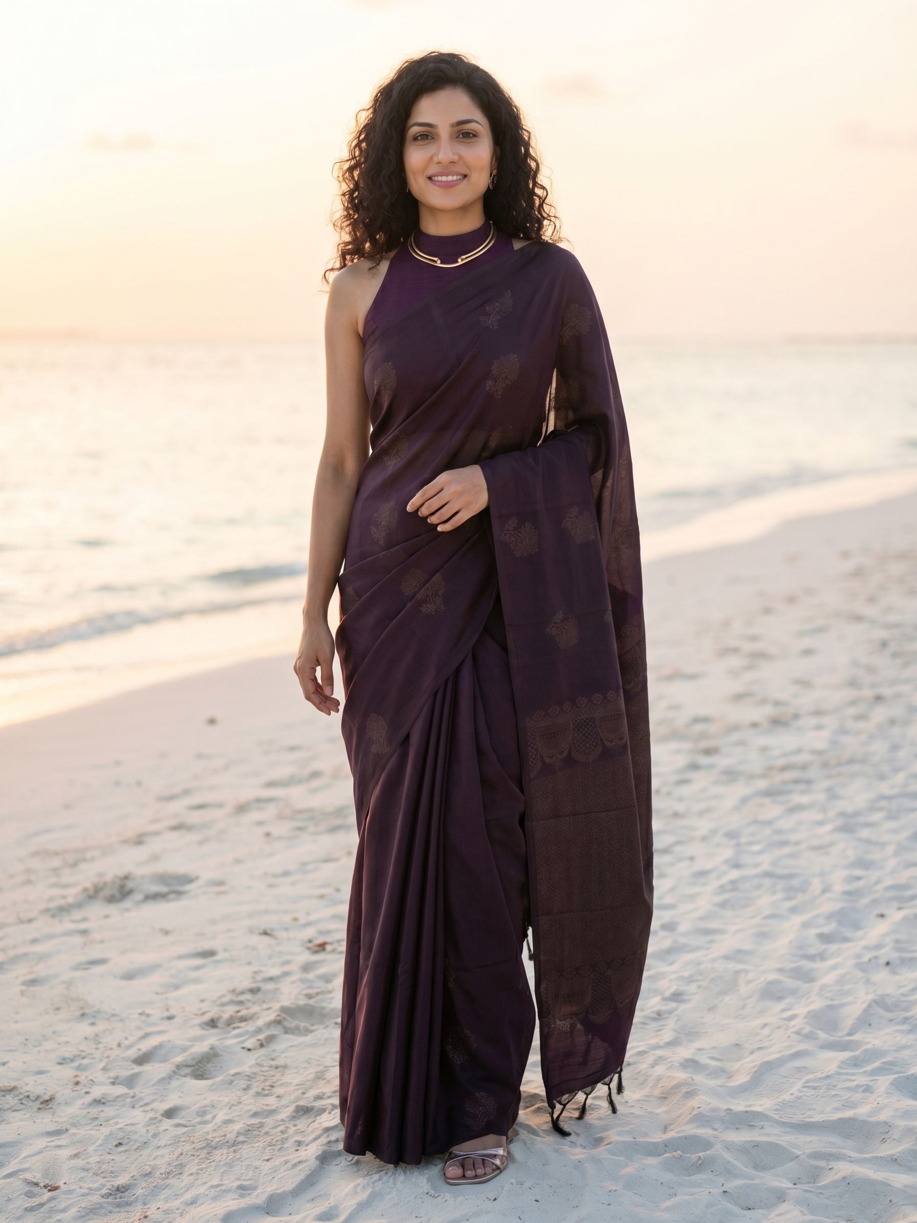Woman in a dark purple saree standing on a beach