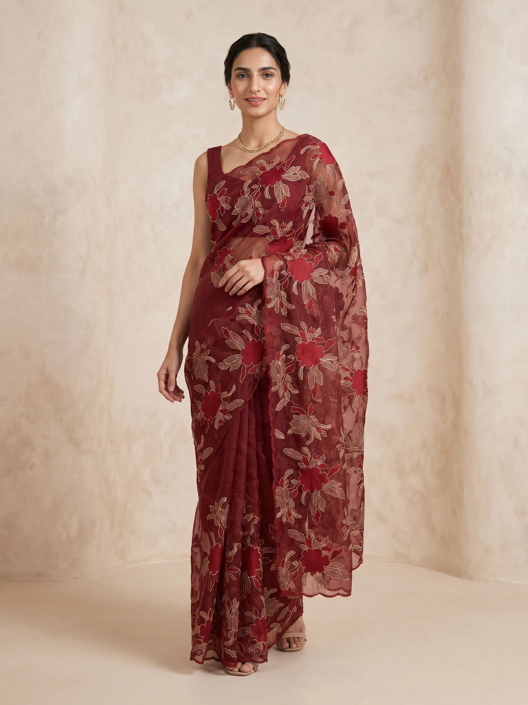 Woman wearing a maroon saree with floral patterns against a beige background