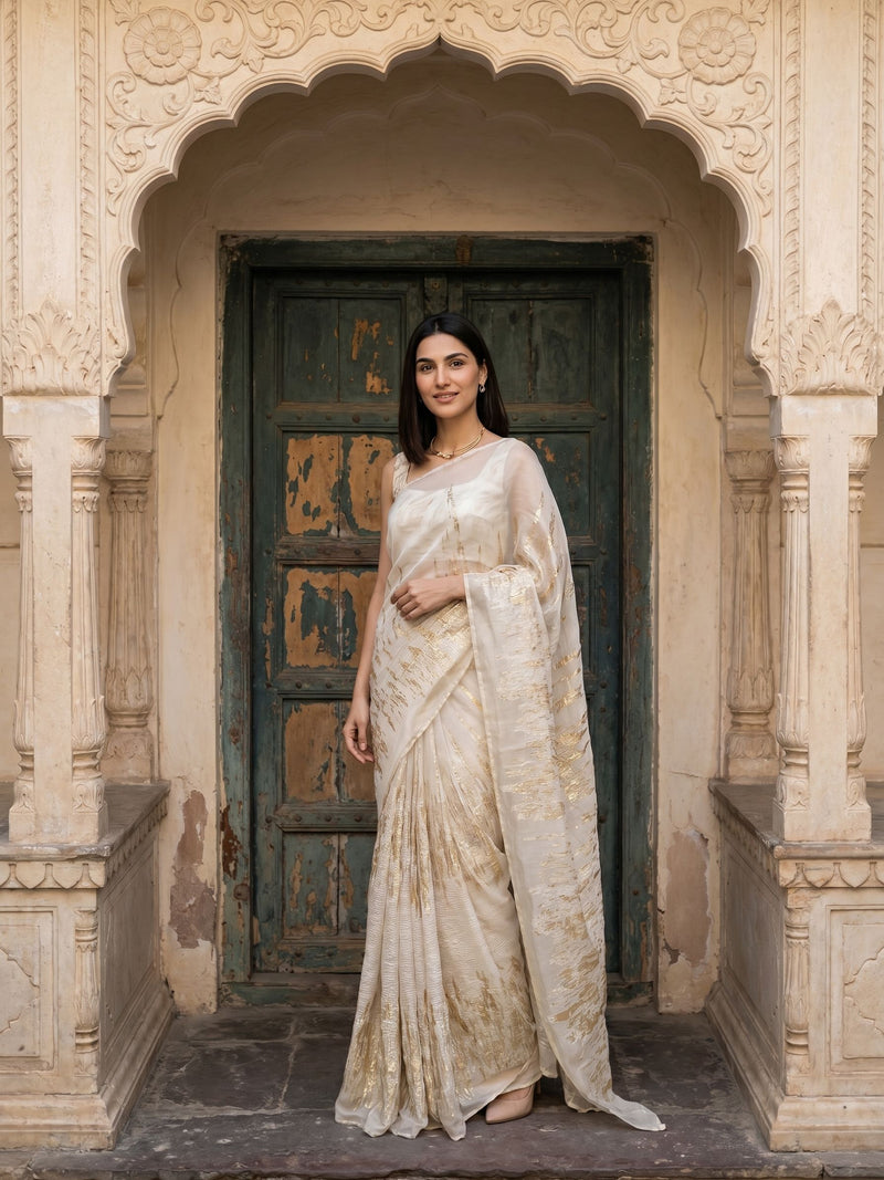 Woman in a white saree standing in front of an ornate archway.
