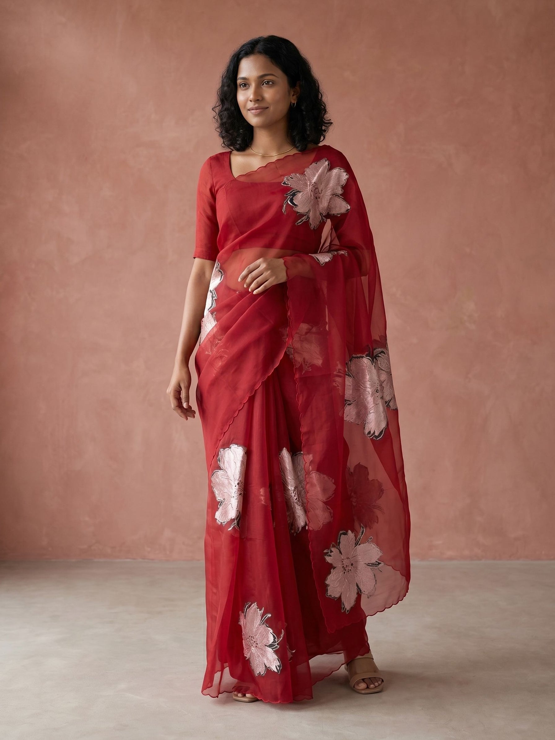 Woman wearing a red saree with floral patterns against a pink background