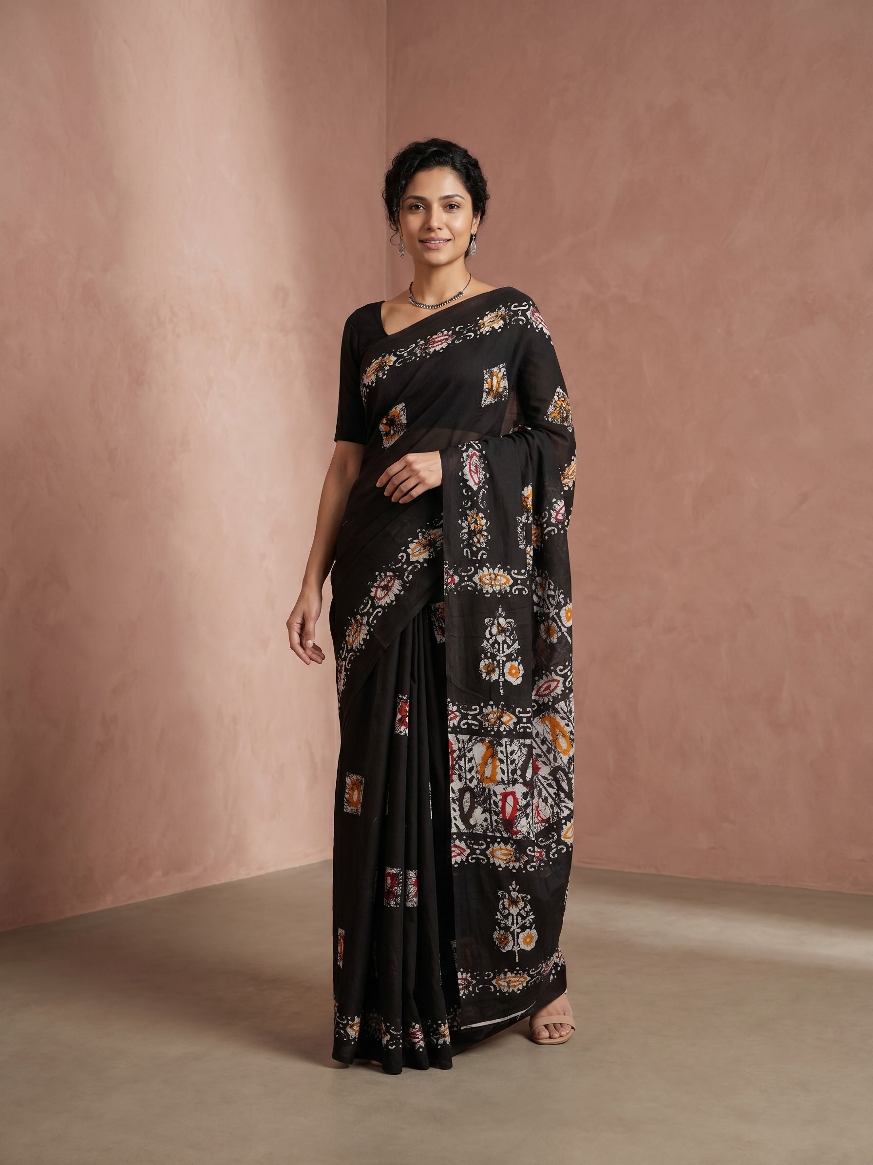 Woman wearing a black saree with floral patterns against a pink background