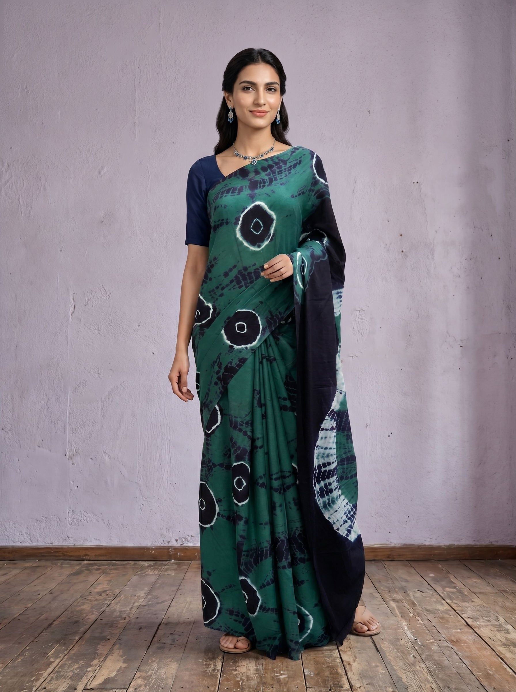 Woman wearing a green and black patterned saree against a plain background