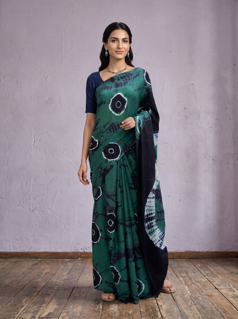 Woman wearing a green and black patterned saree against a plain background