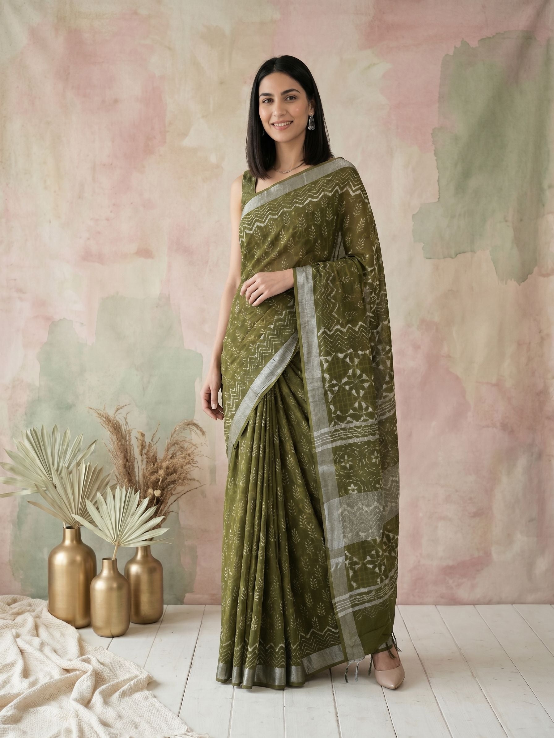 Woman wearing a green saree with a white border against a pastel wall.