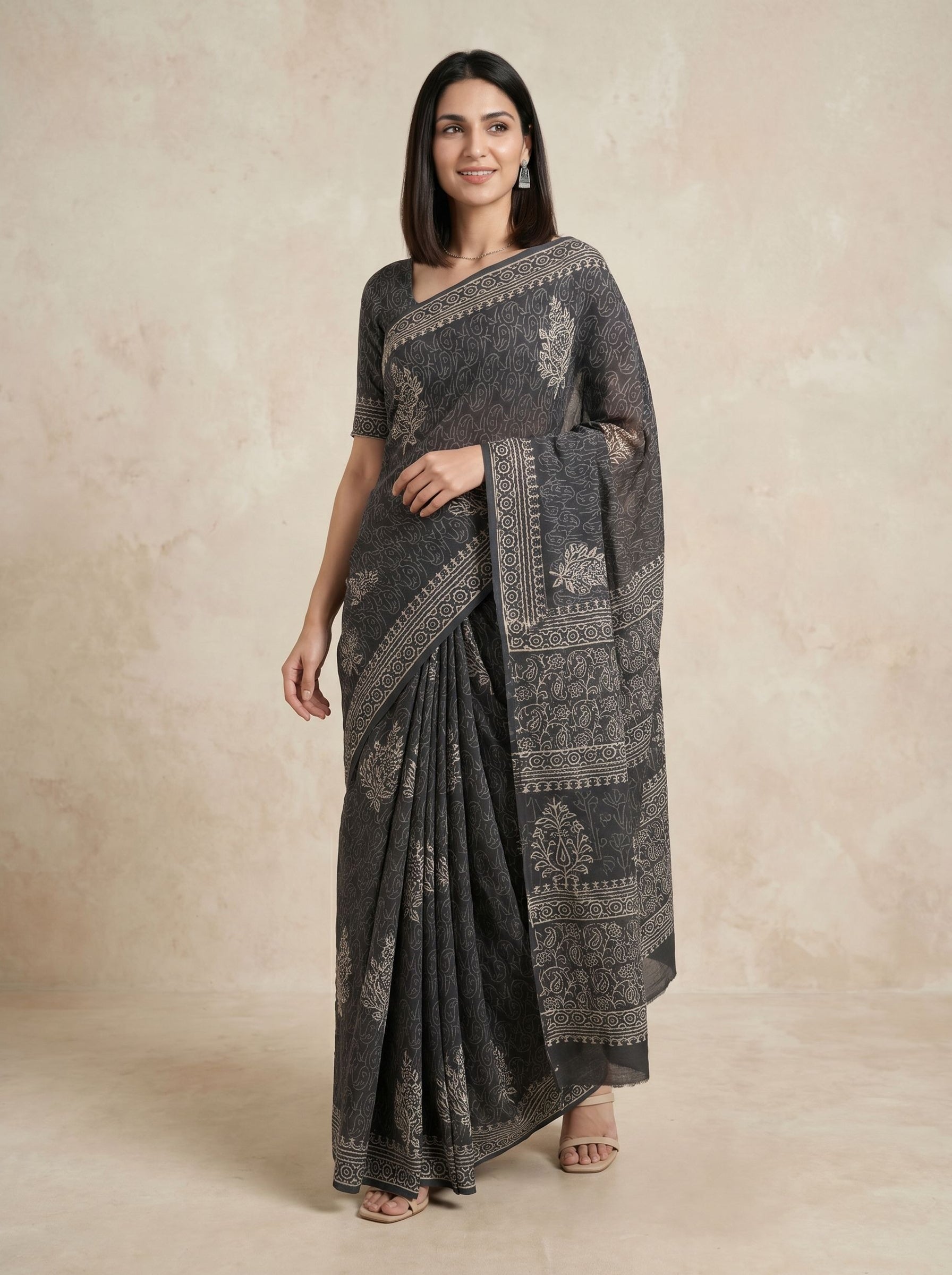 Woman wearing a dark gray saree with intricate patterns on a beige background