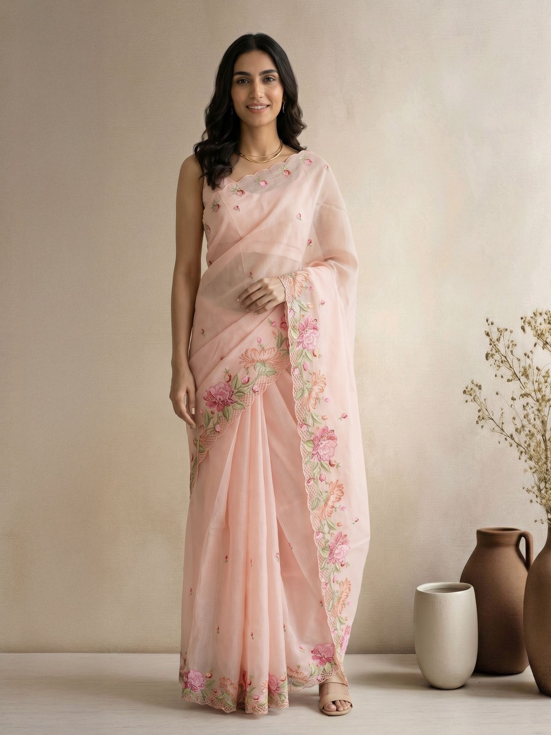 Woman wearing a light pink saree with floral patterns in a minimalistic setting.