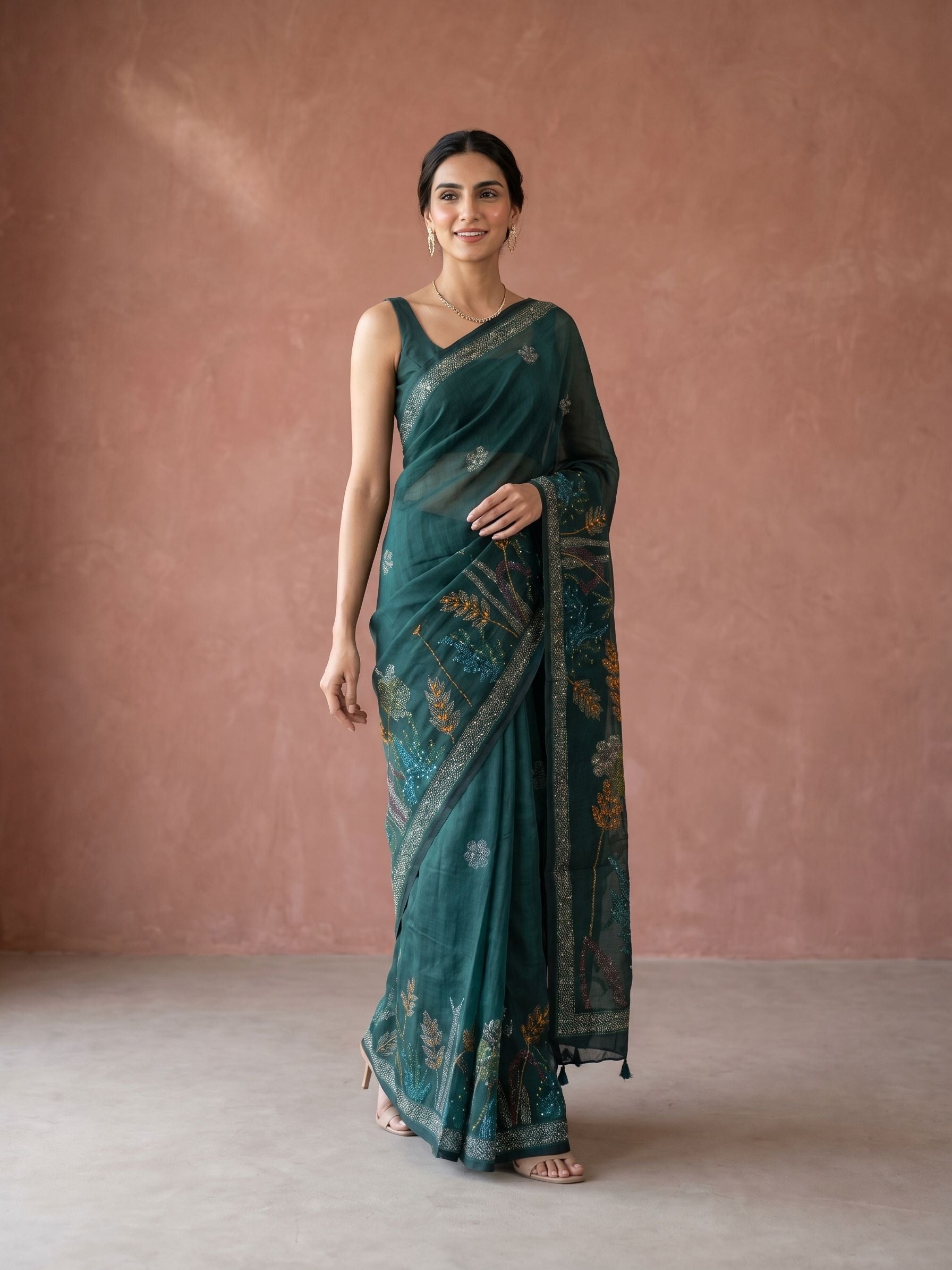 Woman wearing a teal saree with a pattern against a pink wall.