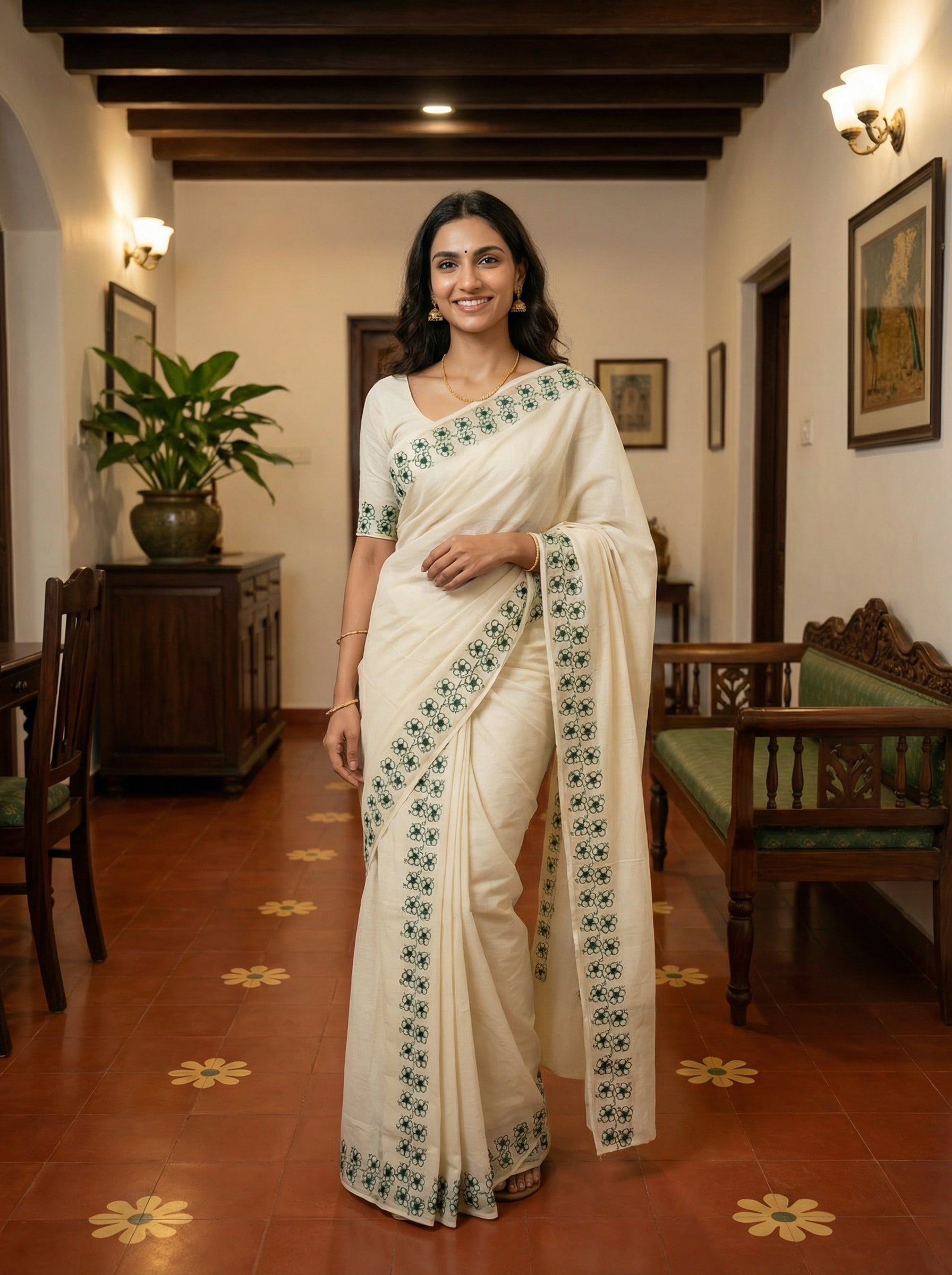Woman in a white saree with green patterns standing in a room with wooden furniture and decorative elements.