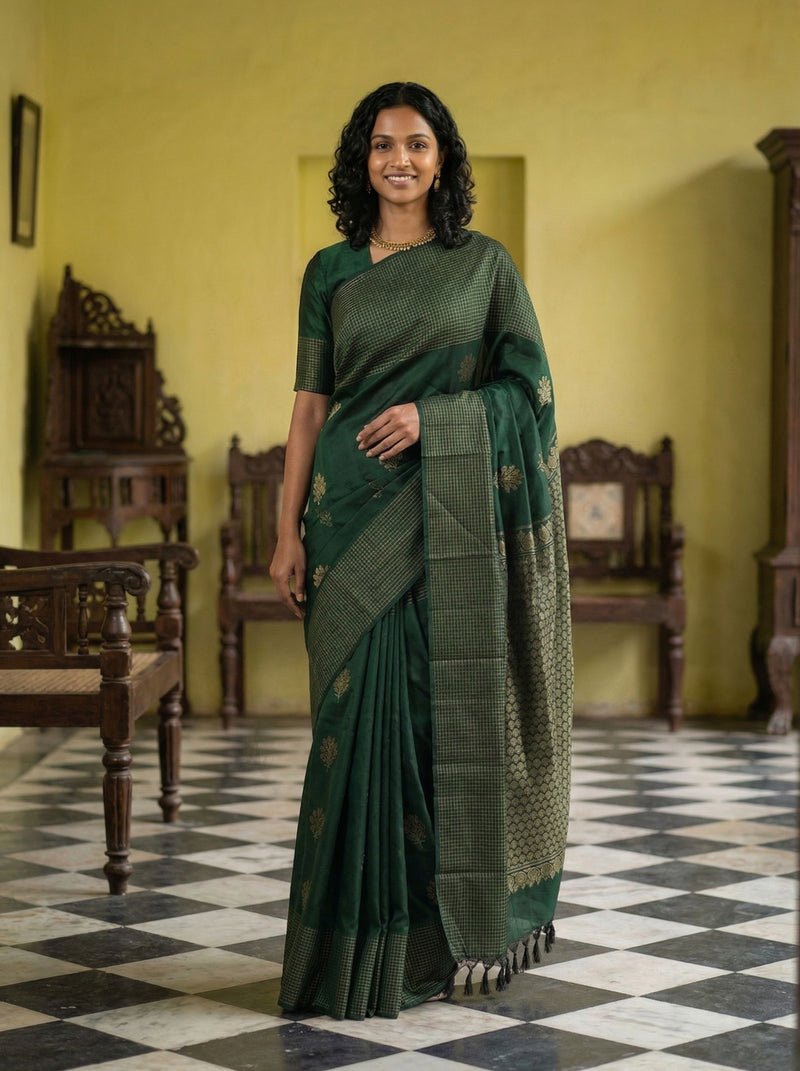 Woman in a green saree standing in a room with checkered floor and wooden furniture.