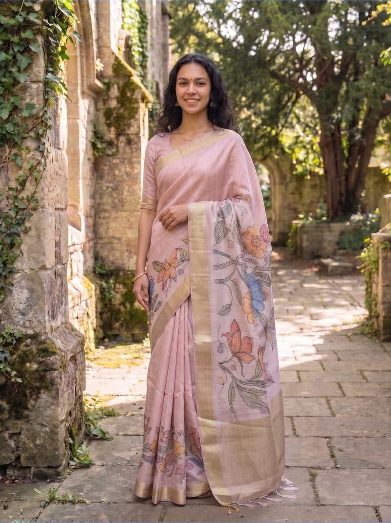 Woman in a pink saree with floral patterns standing outdoors.