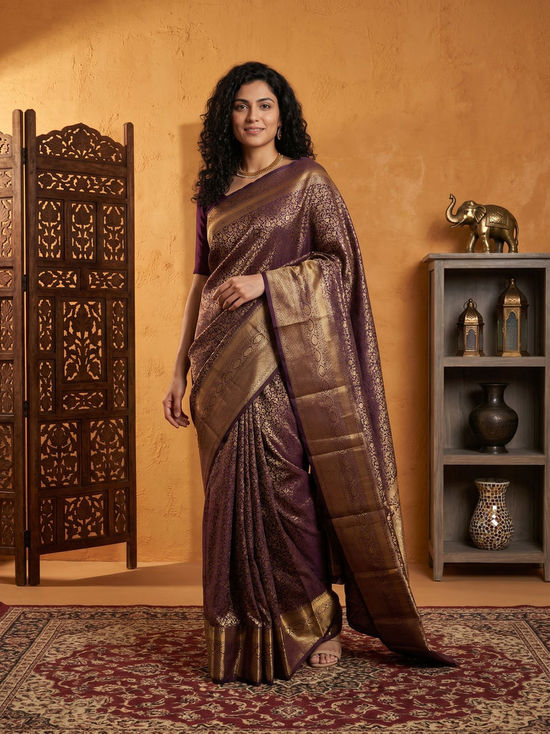 Woman wearing a traditional saree in a decorated room with a wooden screen and shelves.