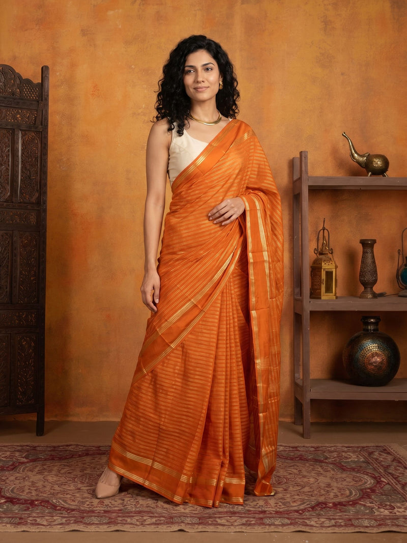 Woman in an orange saree standing against an orange wall with decorative items.