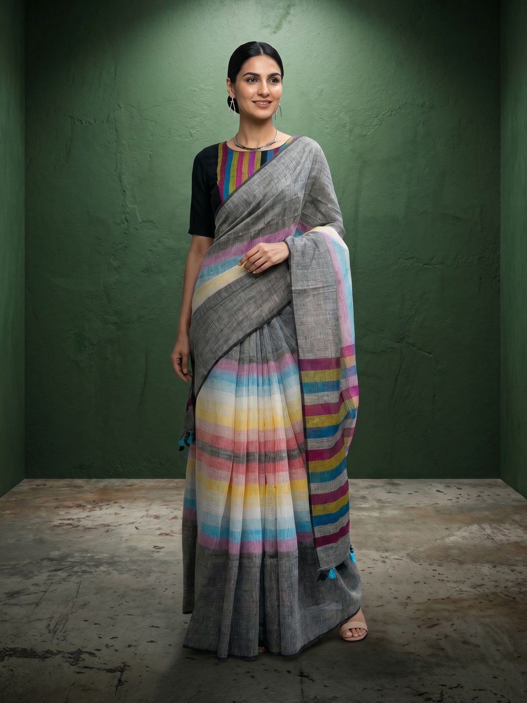 Woman wearing a gray saree with colorful stripes against a green wall.