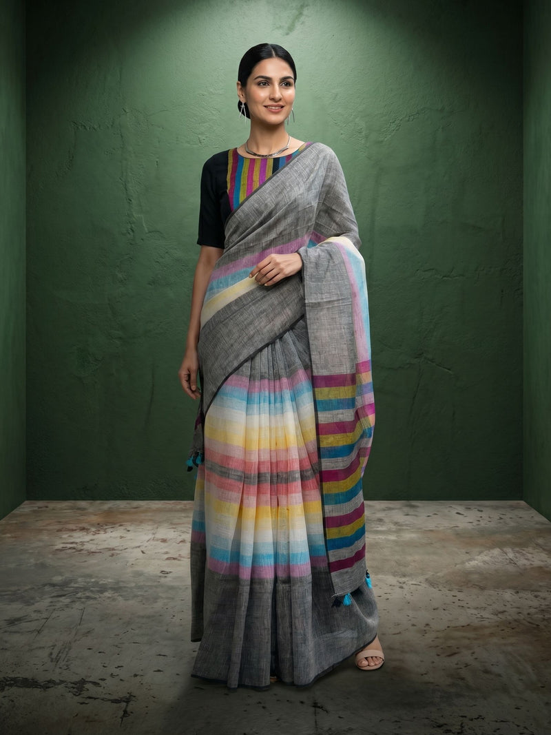 Woman wearing a gray saree with colorful stripes against a green wall.