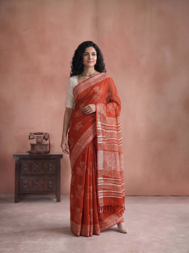 Woman wearing a red saree with a white blouse against a beige wall.