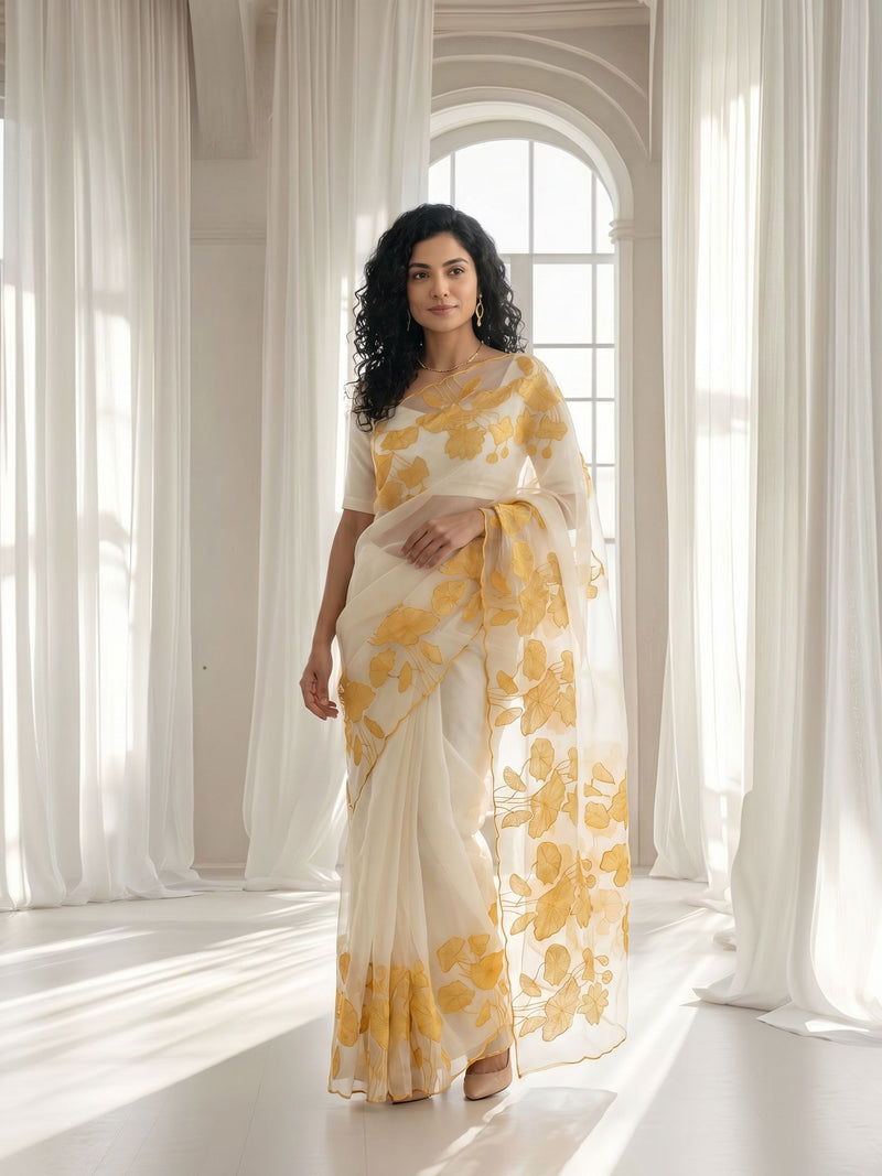 Woman wearing a white saree with yellow floral patterns in a bright room.