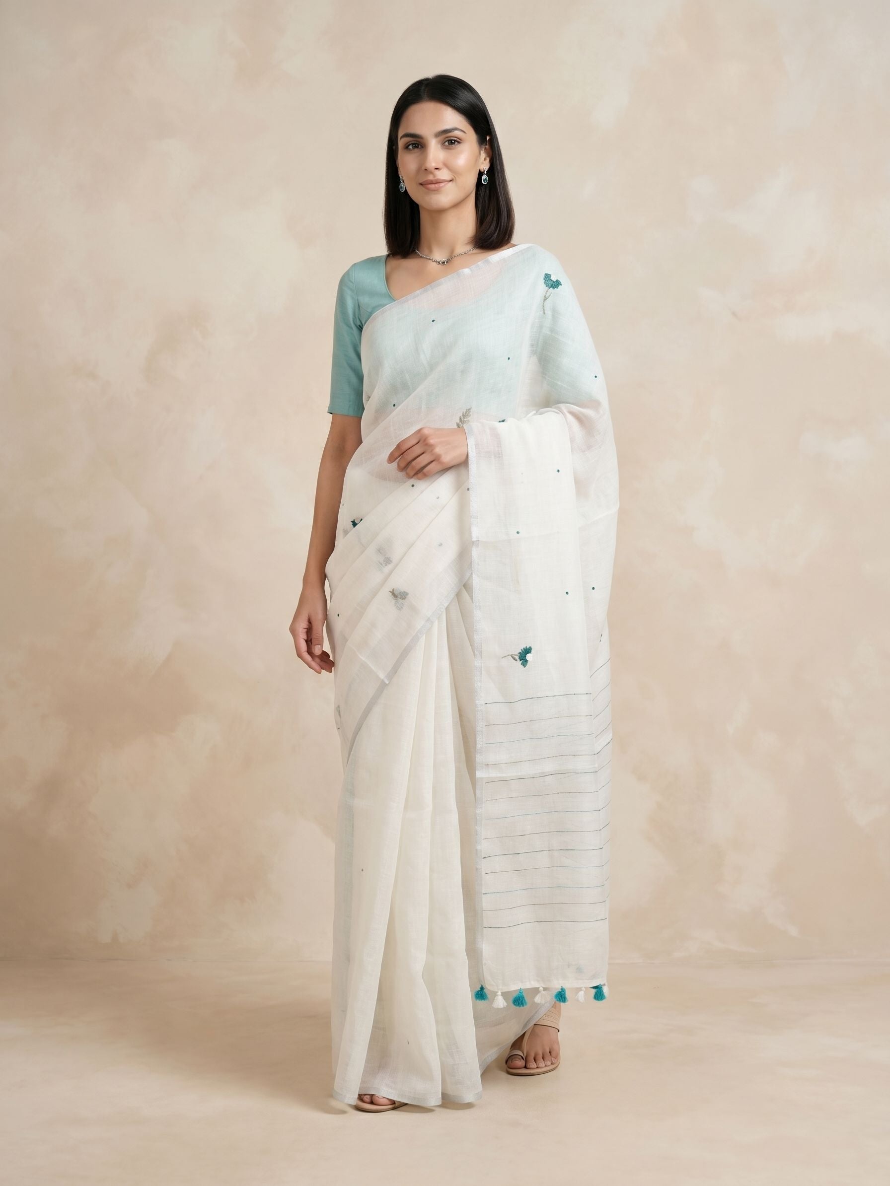 Woman wearing a white saree with a blue blouse against a beige background