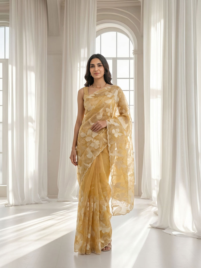 Woman in a yellow saree standing in a bright room with white curtains.
