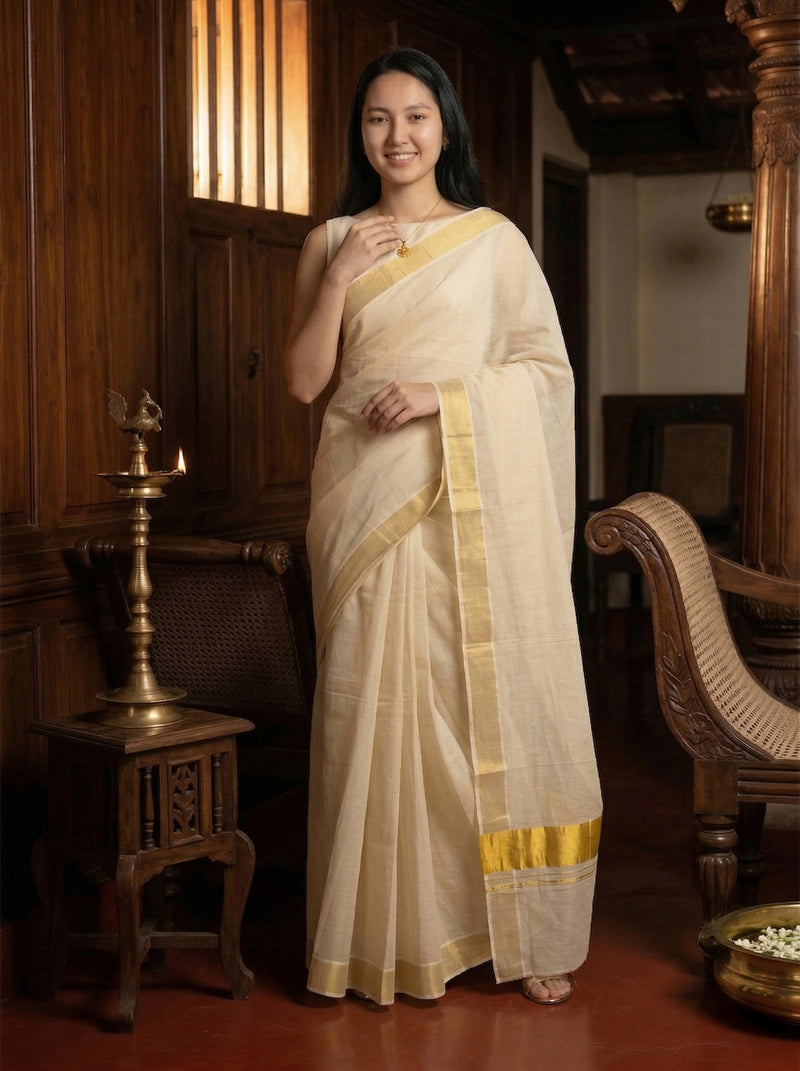 Woman in a white saree with gold border standing in an ornate room.