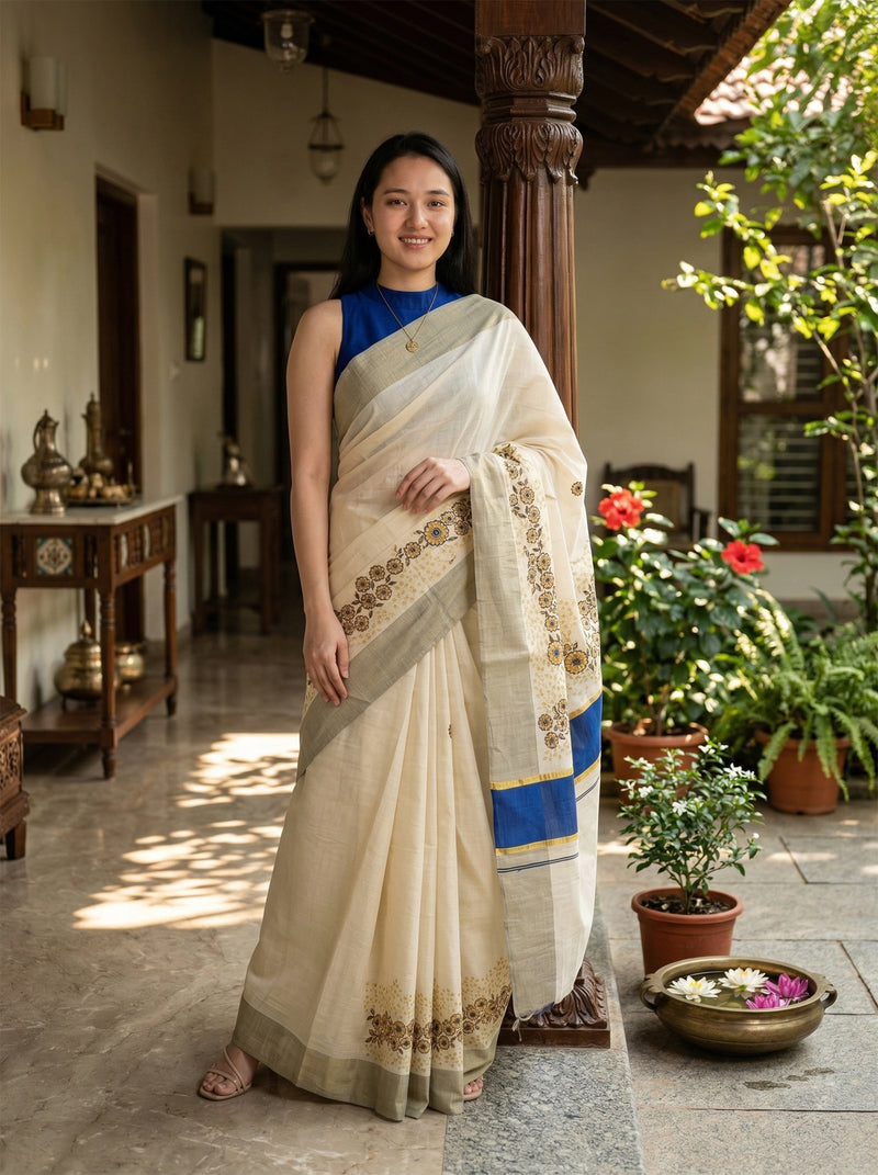 Woman in a white saree with blue accents standing in a sunlit room with plants.