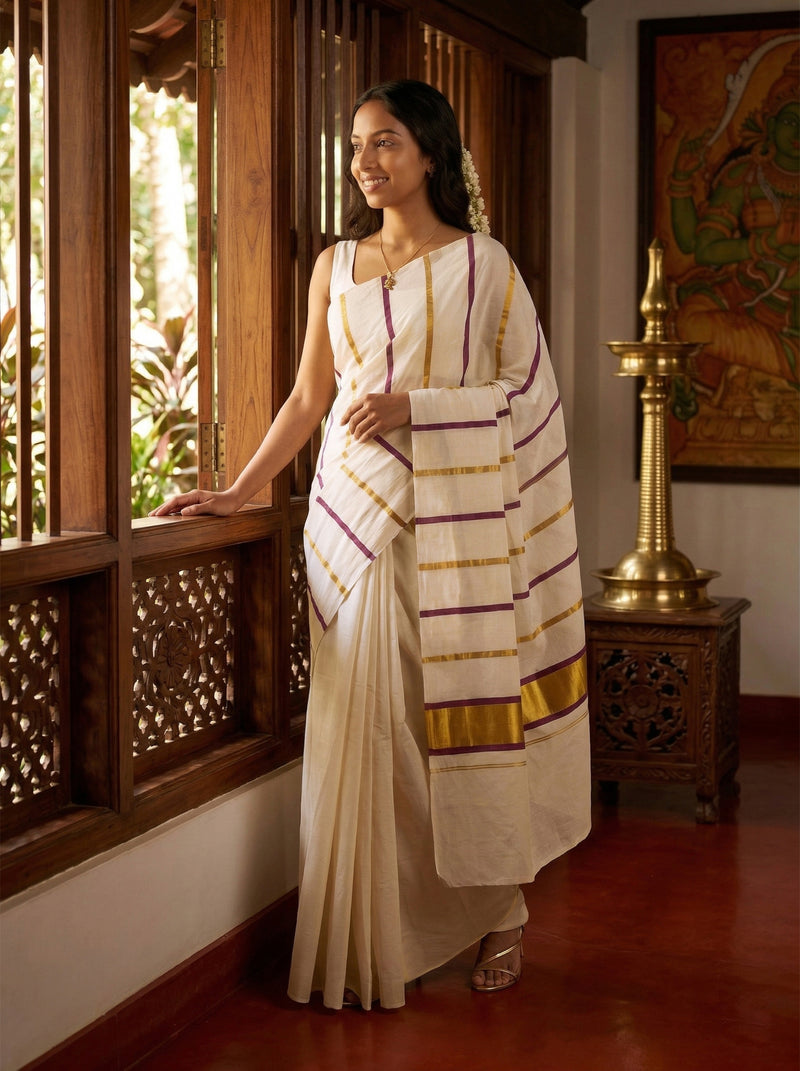 Woman in a traditional white saree with gold and red border standing in a room with wooden window and decorative elements.