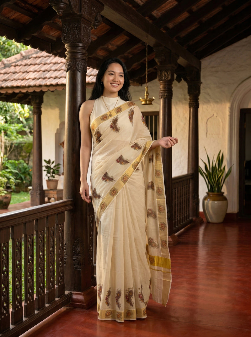Woman in a traditional saree standing in a decorative indoor setting with wooden pillars and plants.