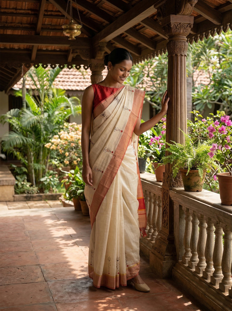 Woman in a white saree with a red blouse standing in a garden setting.