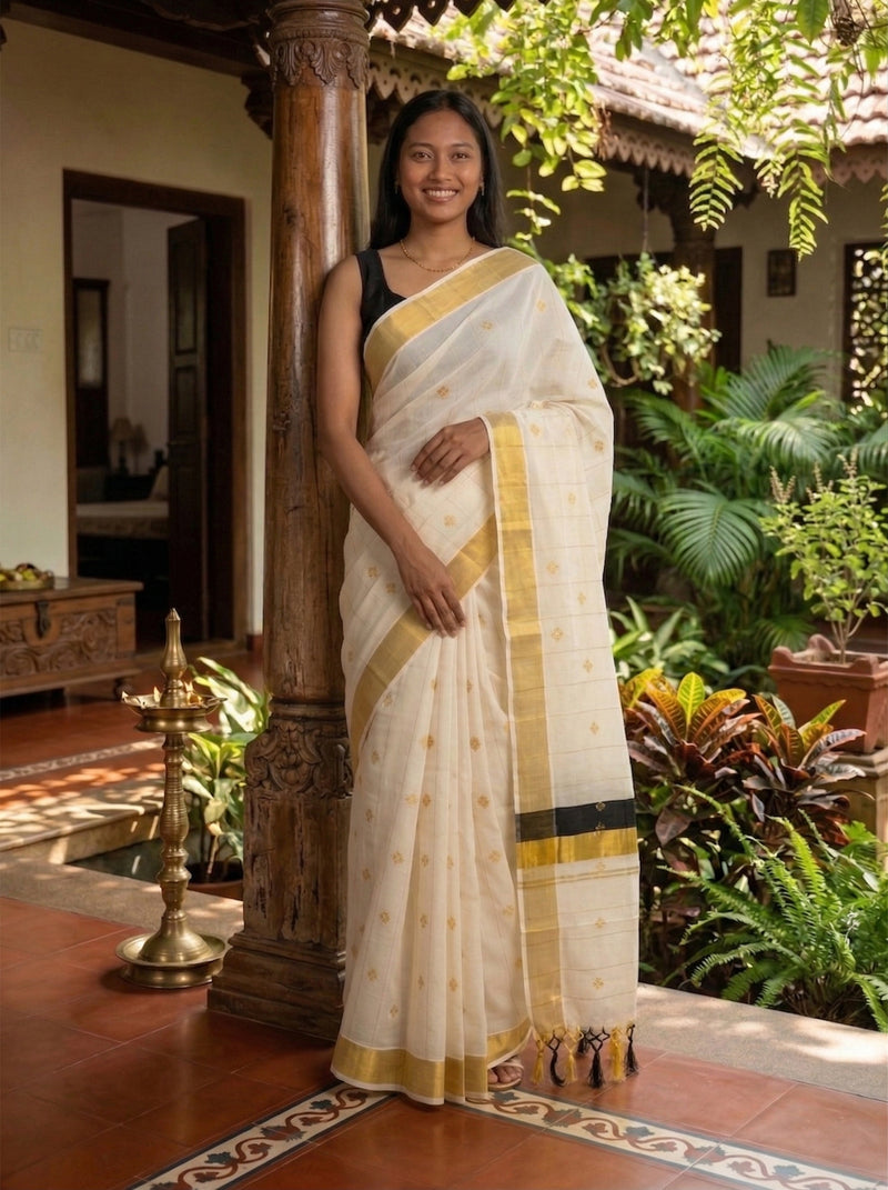 Woman in a white saree with gold border standing in a garden setting