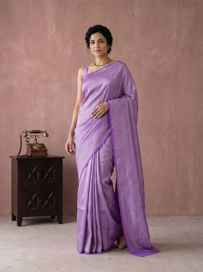 Woman wearing a purple saree standing against a plain background