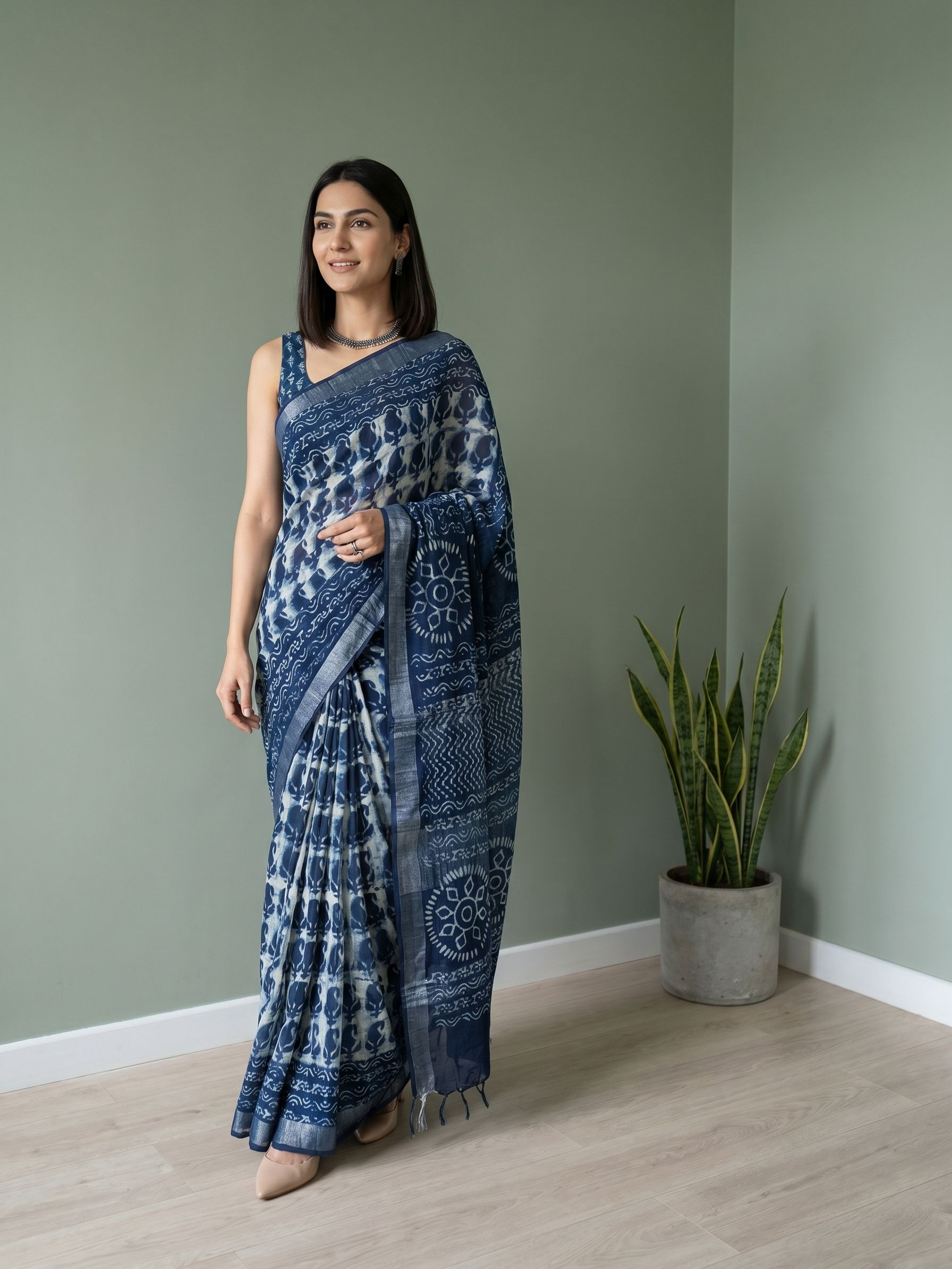 Woman wearing a blue and white saree standing in a room with a plant.