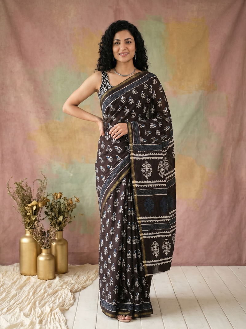 Woman wearing a black saree with white patterns, standing in front of a colorful curtain.