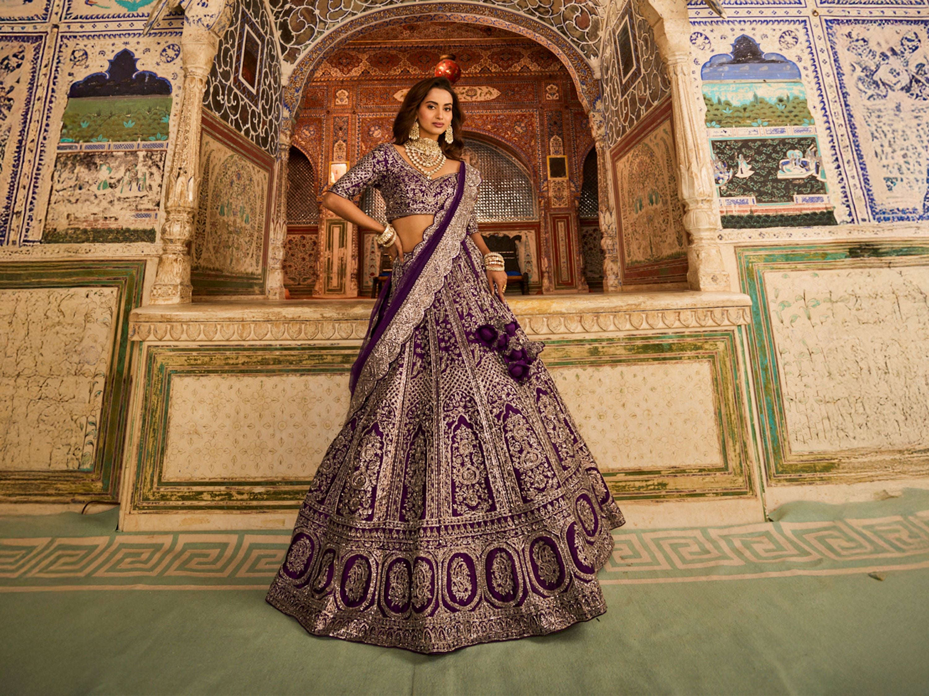 Woman in a purple traditional outfit standing in an ornate decorated room - Kalyan Silks.