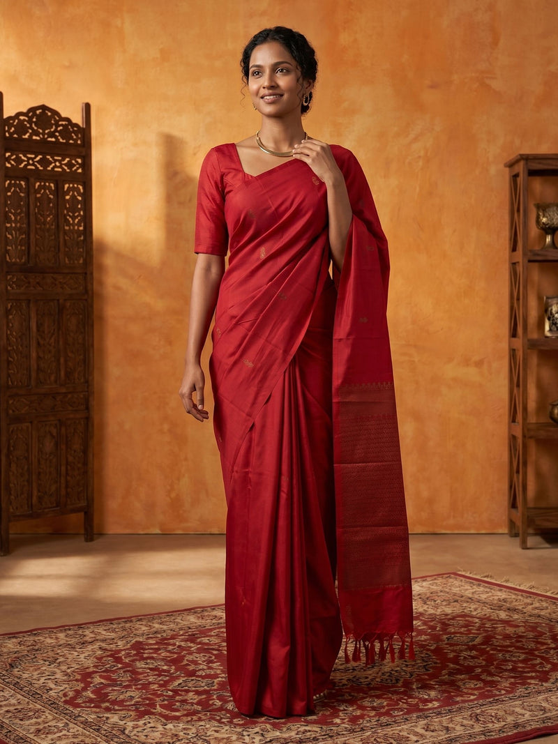 Woman in a red saree standing against an orange wall.