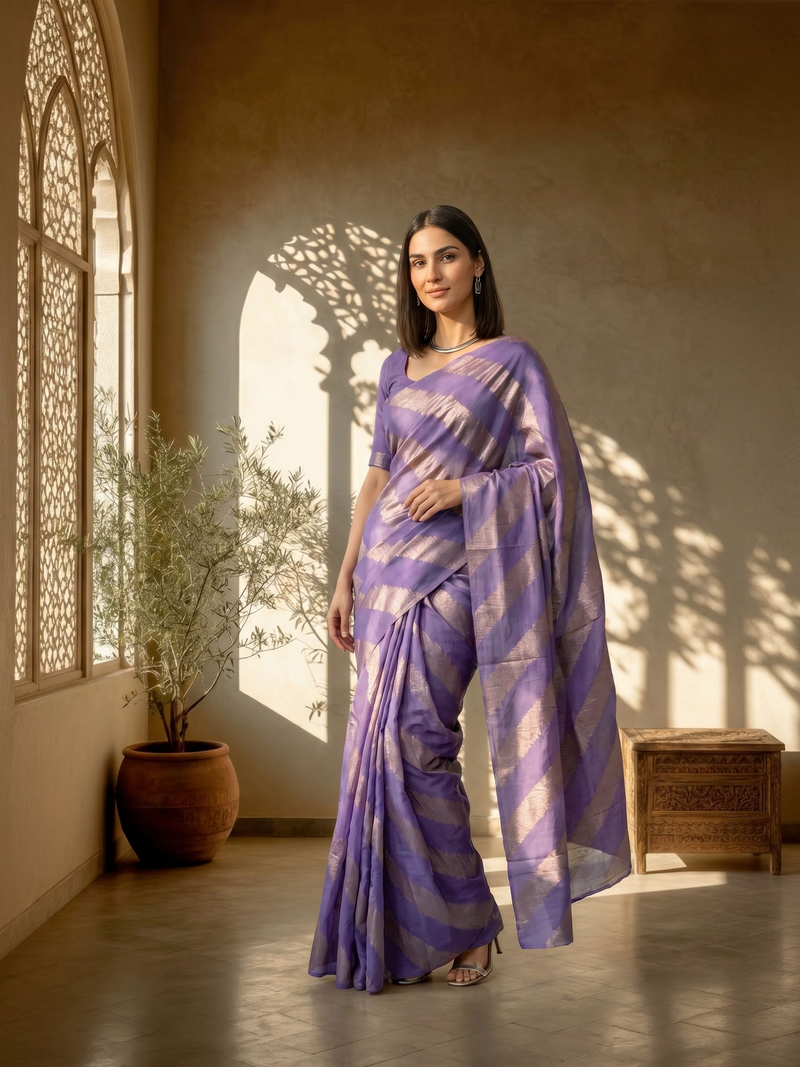 Woman in a purple saree standing in a sunlit room with architectural elements.