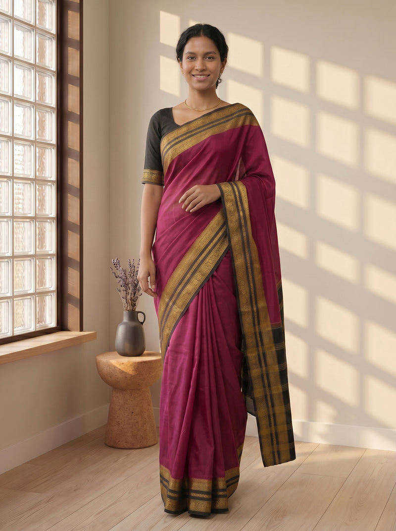 Woman wearing a magenta saree with gold border indoors near a window.