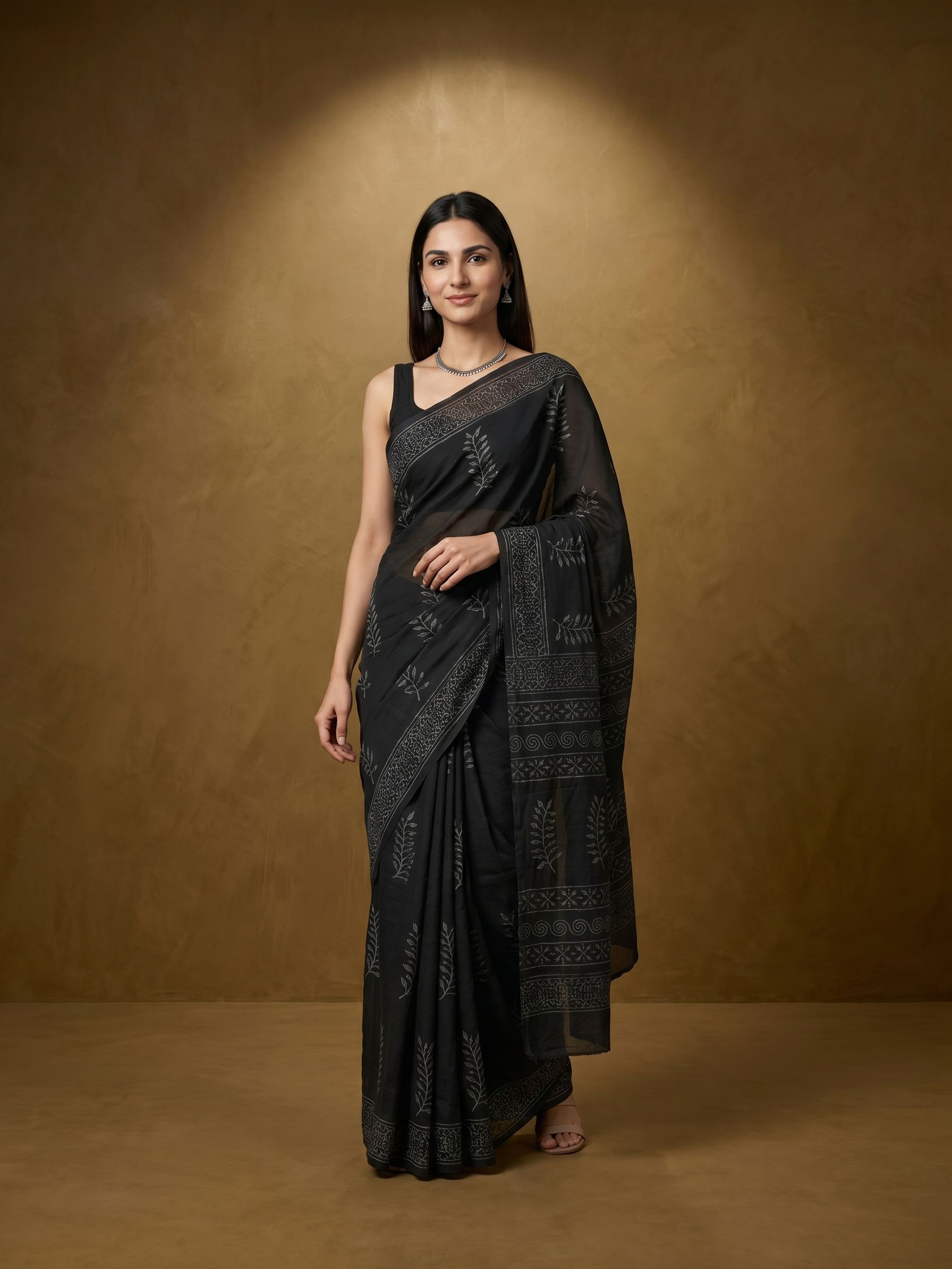 Woman wearing a black saree with intricate patterns against a brown background