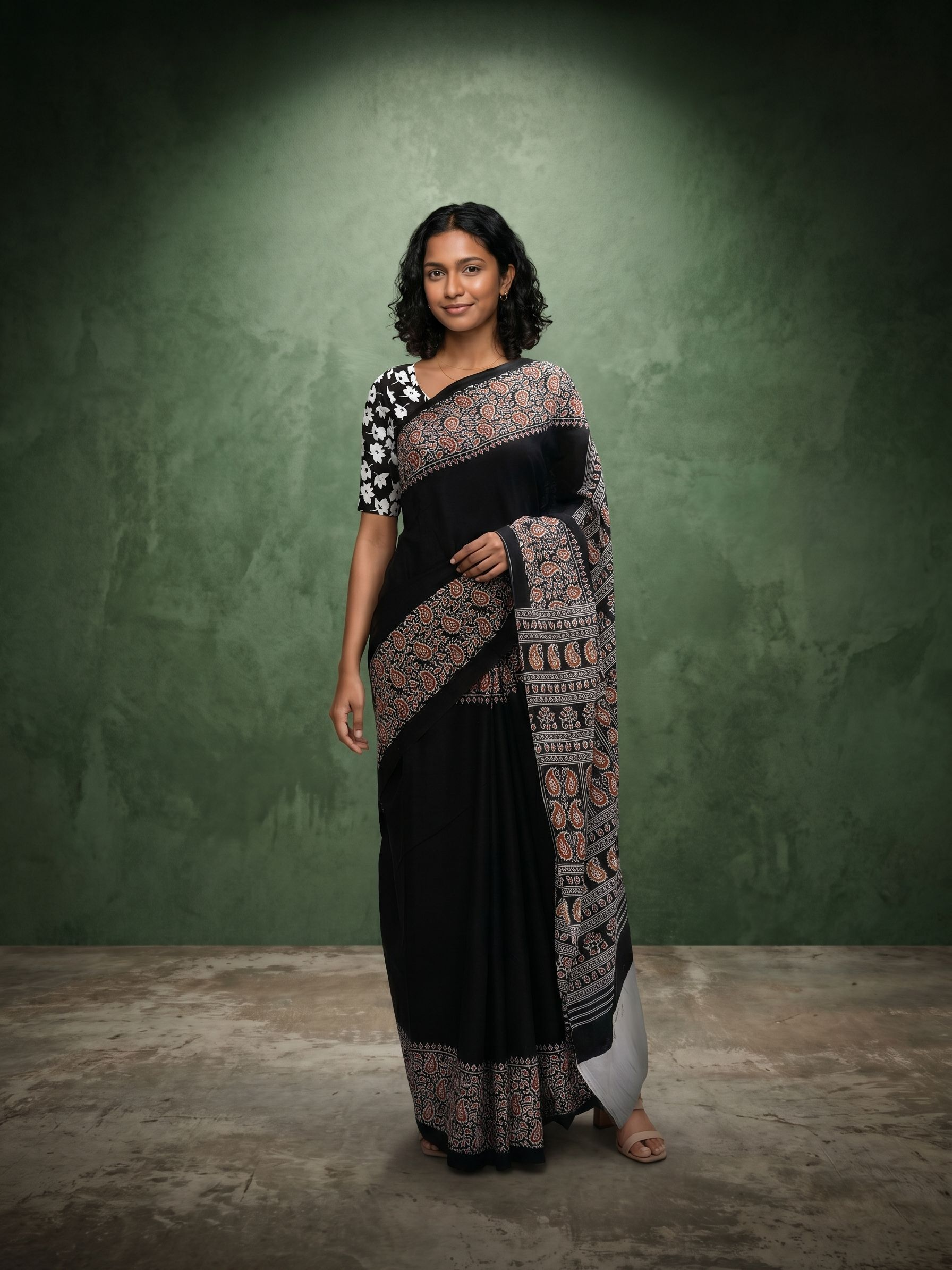 Woman wearing a black and patterned saree against a green background