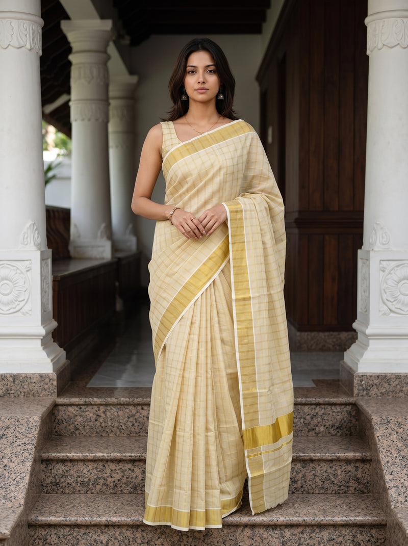 Woman in a traditional cream saree with gold border standing on steps.