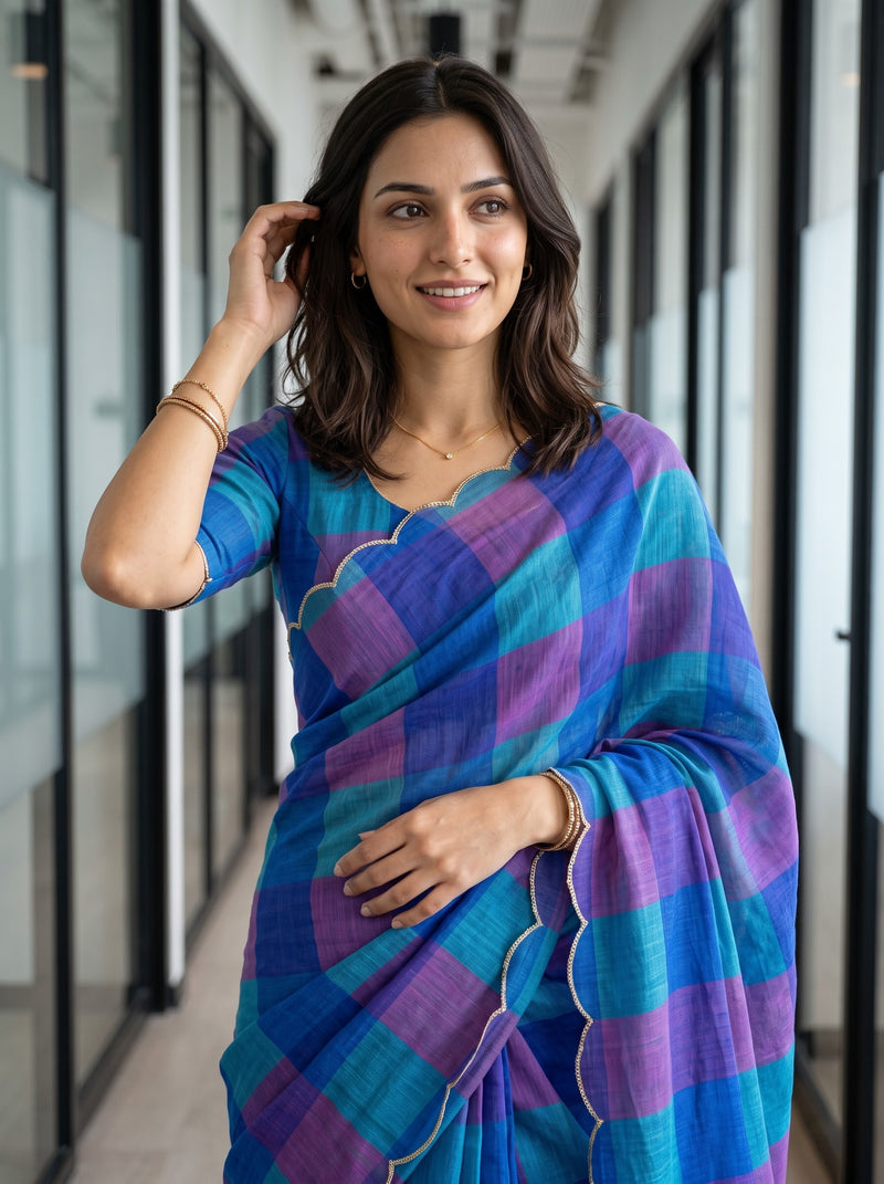 A woman wearing a blue and purple checkered saree with a scalloped border, standing in a modern office hallway.
