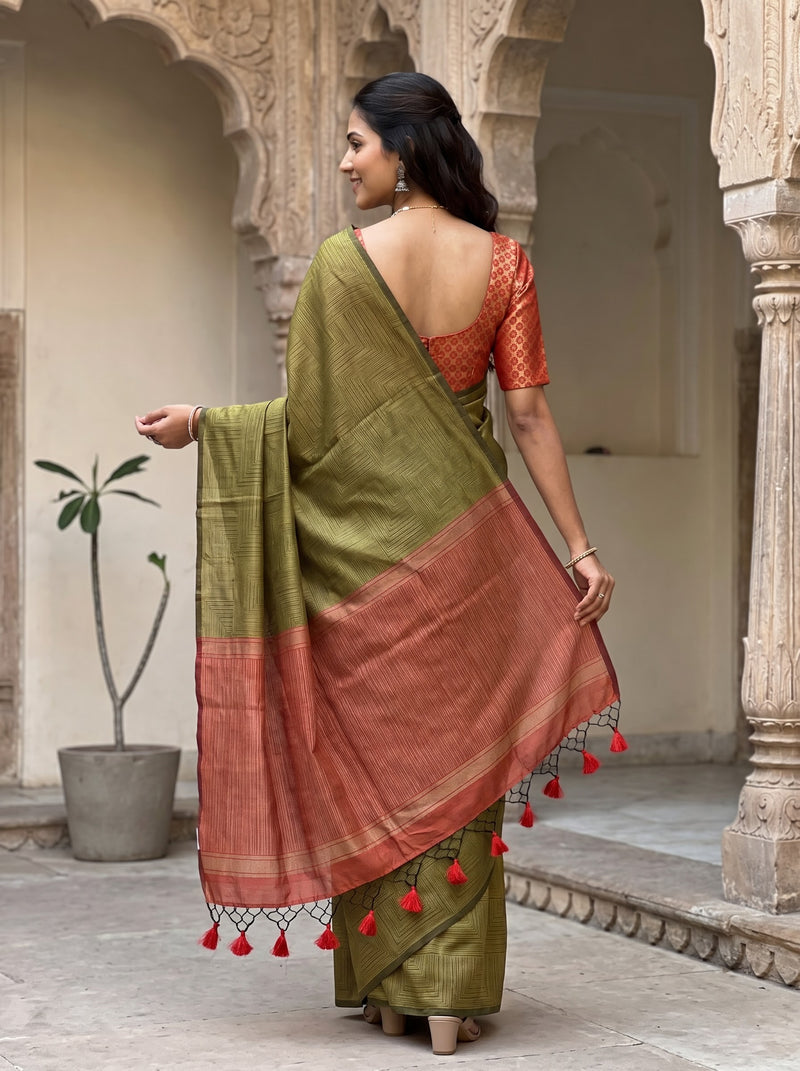 A woman wearing a green and terracotta saree with red tassels, standing in a stone courtyard with arches.
