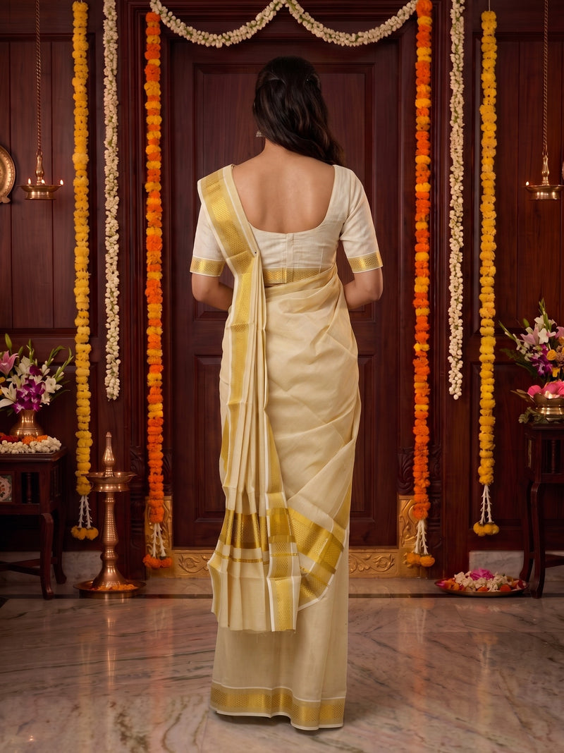 A woman viewed from behind wearing a cream and gold saree with a white blouse, standing in a decorated indoor setting with marigold garlands and a dark wooden door.