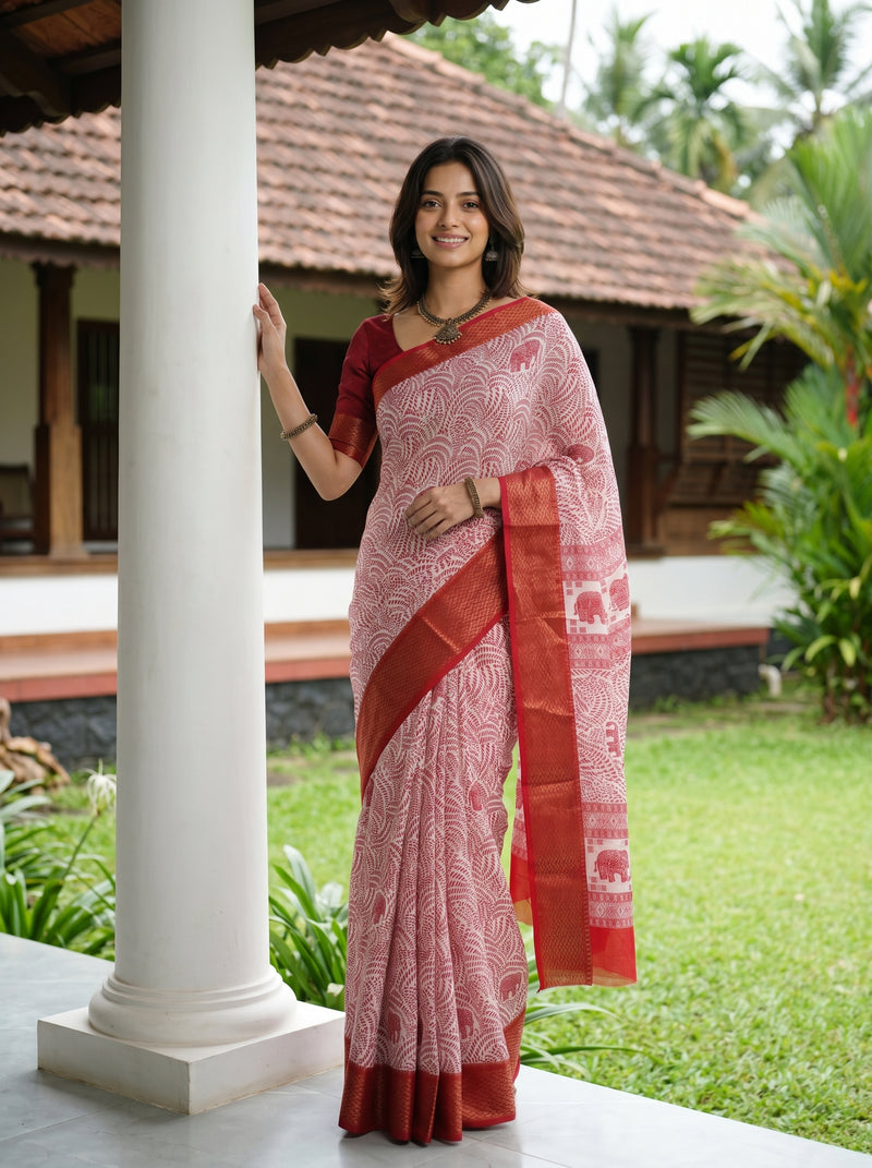 Woman in a traditional saree standing outdoors near a house with greenery.