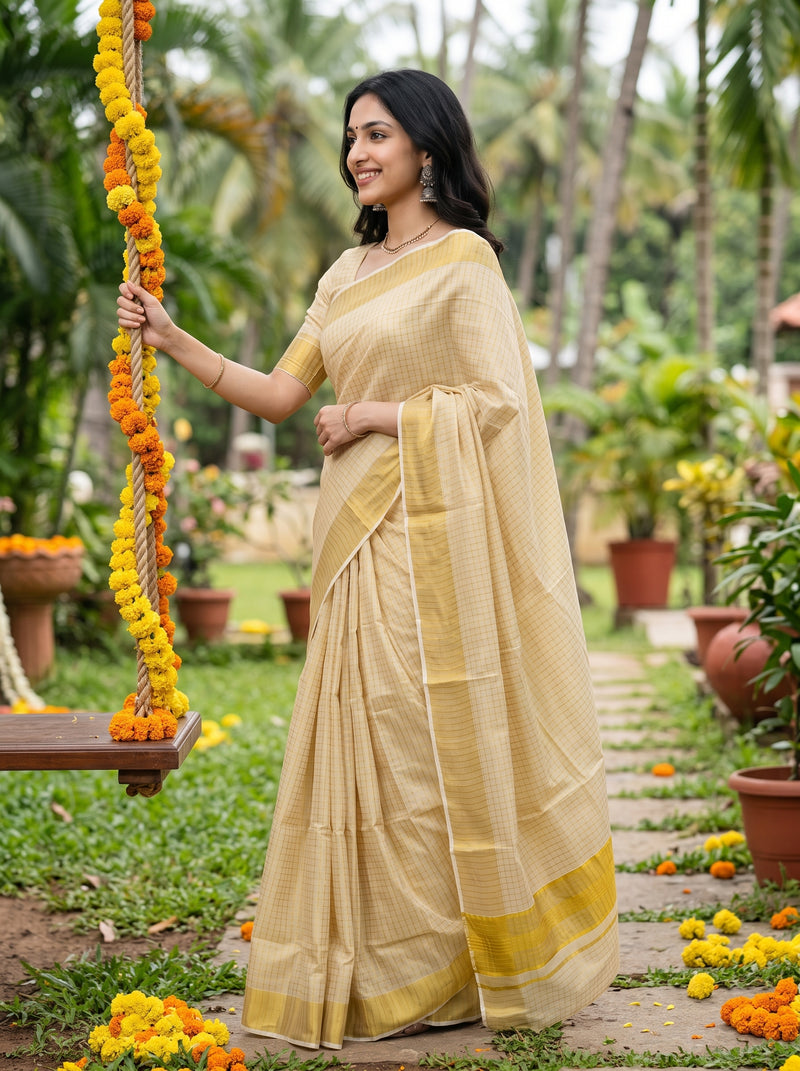A woman wearing a light beige saree with a yellow border stands in a garden next to a swing decorated with marigold garlands.