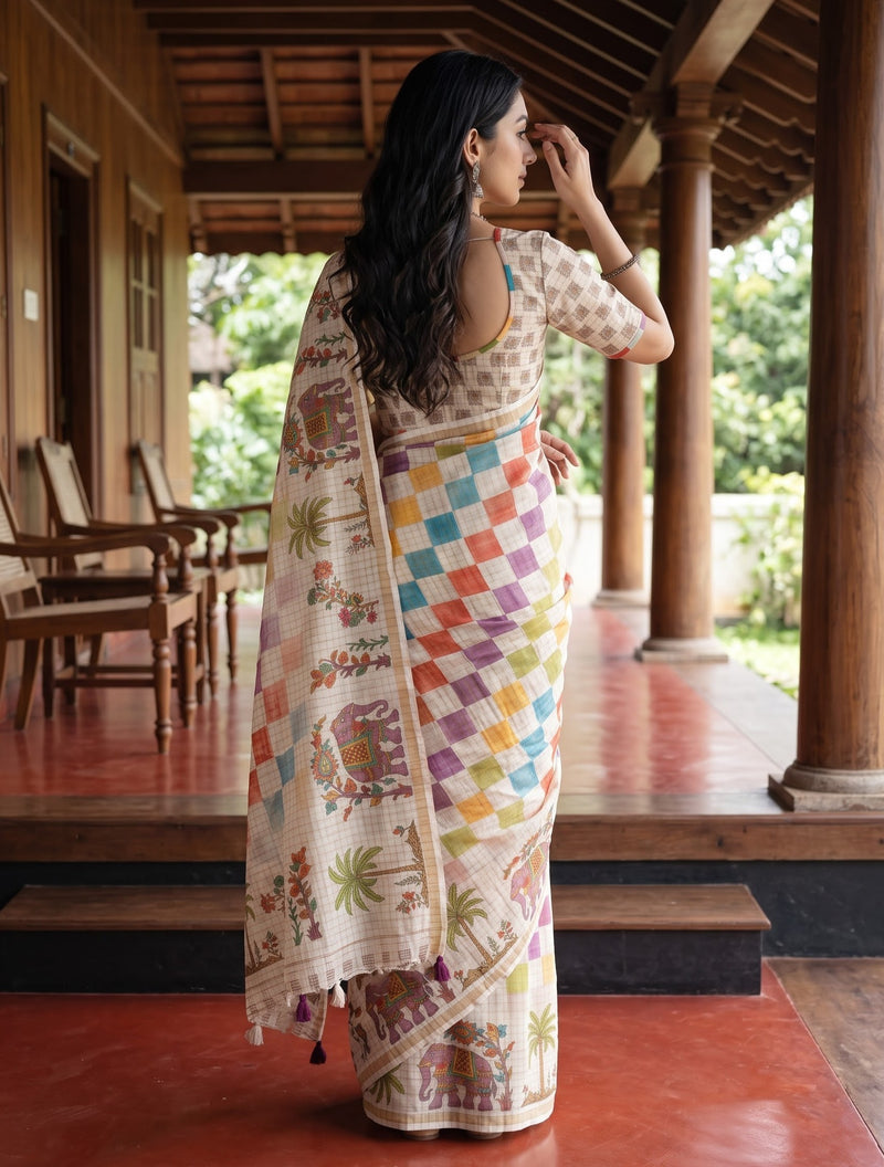 A woman stands on a wooden porch wearing a multicolor patterned saree with a checkered design and floral motifs, paired with a matching printed blouse.