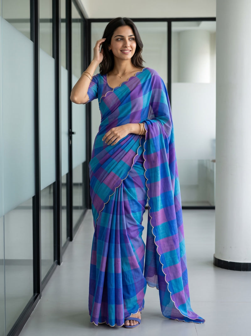 A woman wearing a blue and purple striped saree with a matching blouse, standing in a modern indoor hallway with glass walls.